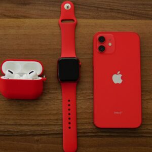 Red Apple iPhone, AirPods, and Apple Watch arranged on a wooden table.